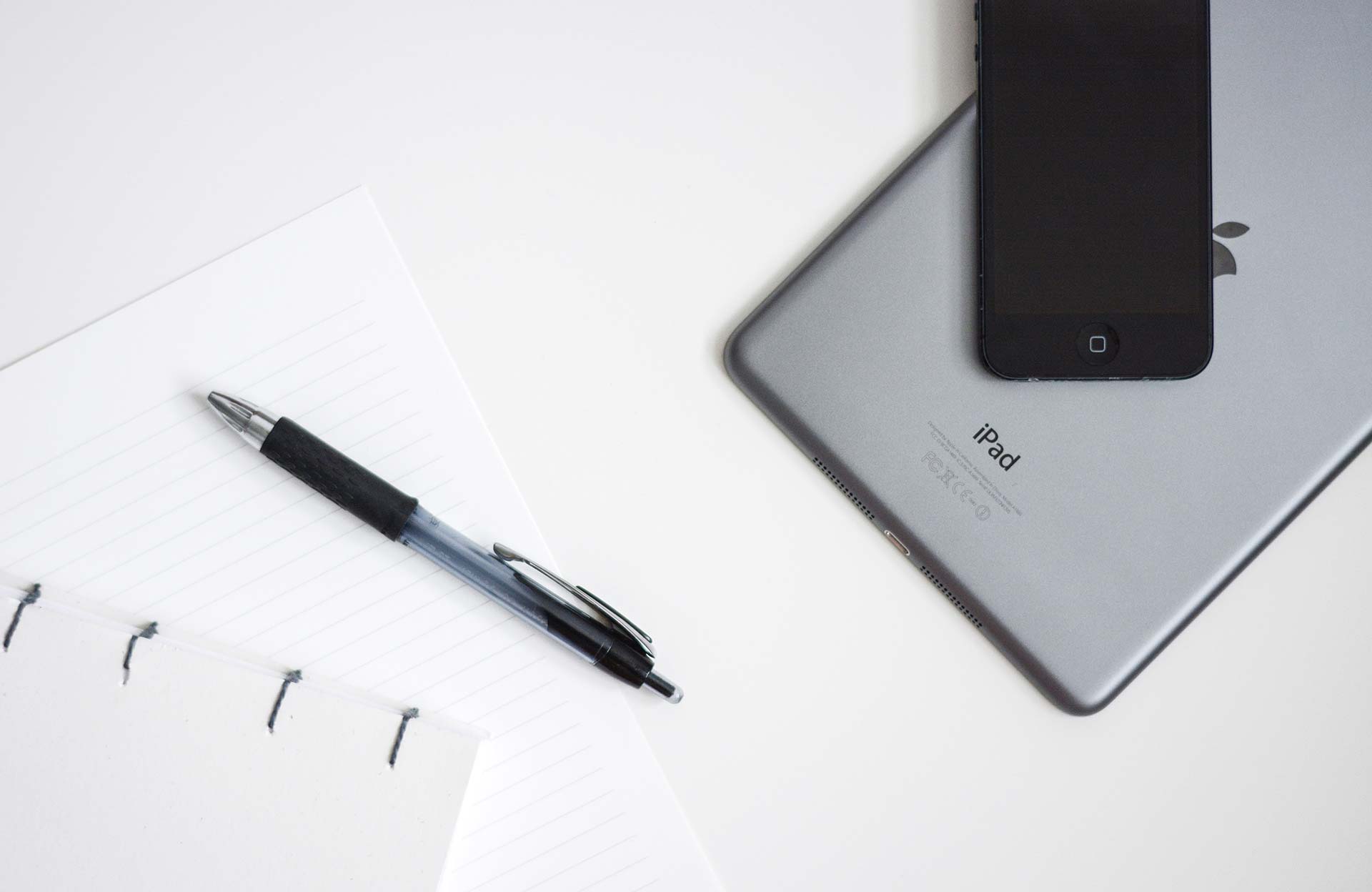 Smartphone, tablet, pen, and notebook on table.